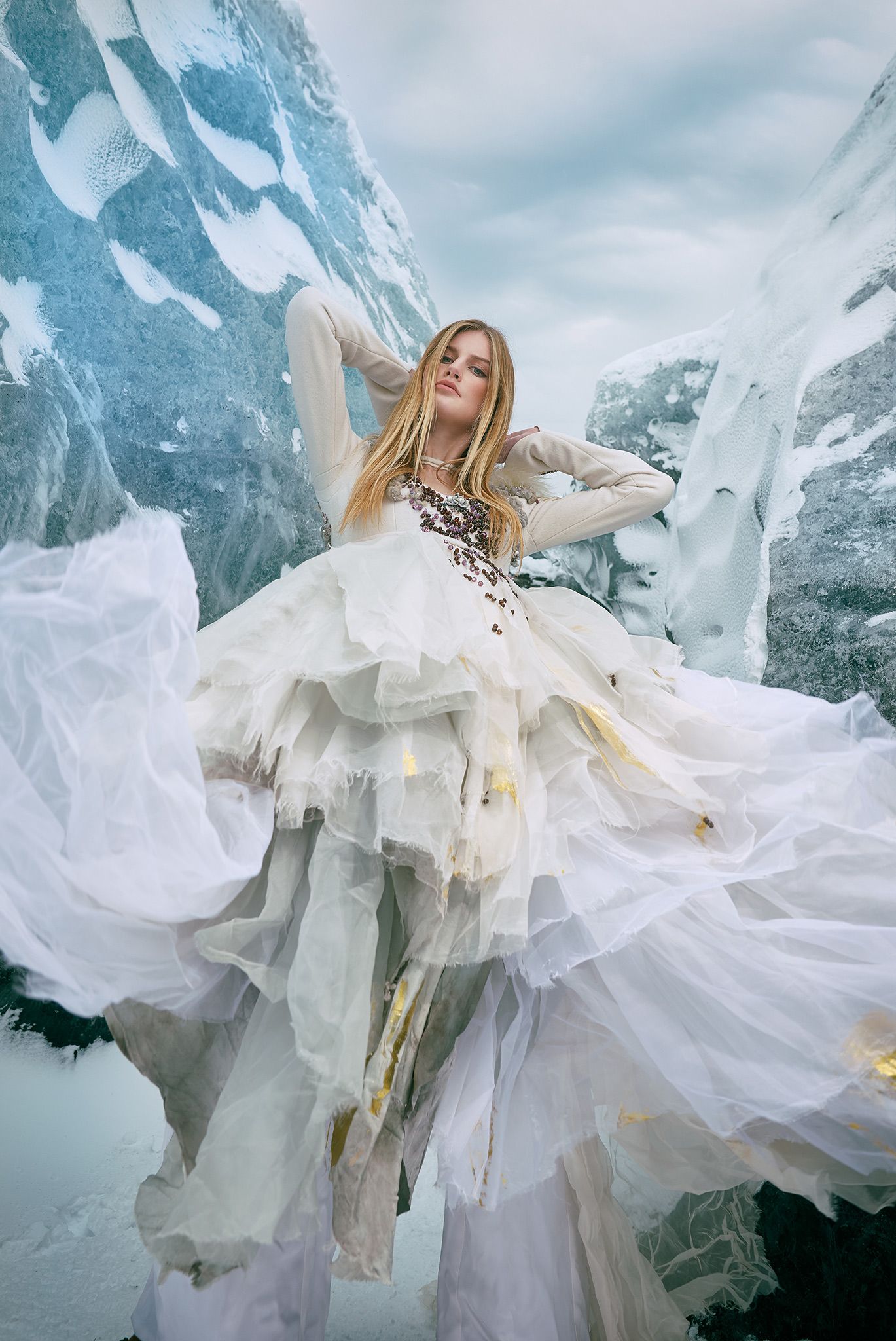 A flowing white dress billows dramatically against a snowy mountain backdrop in an ethereal fashion photoshoot.