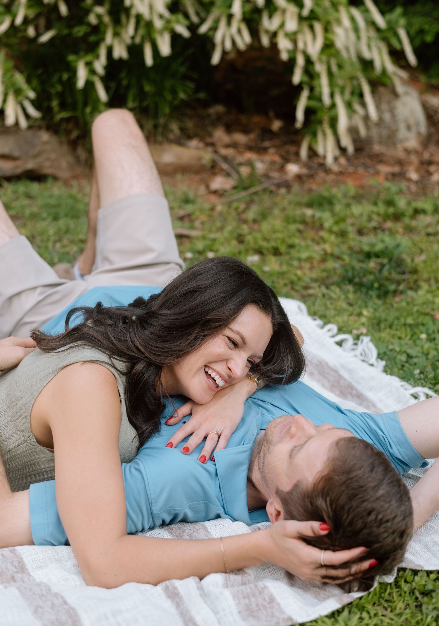 Two people lying together on a picnic blanket outdoors while sharing a tender, joyful moment in the grass.