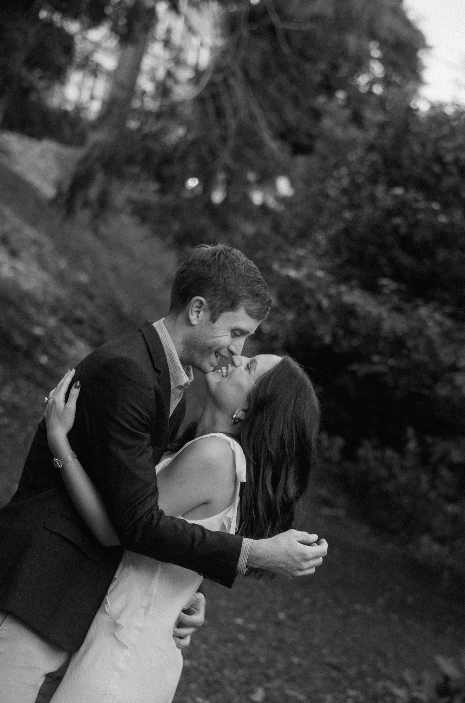 A romantic black and white moment captured of a couple's tender embrace and kiss in a garden setting.