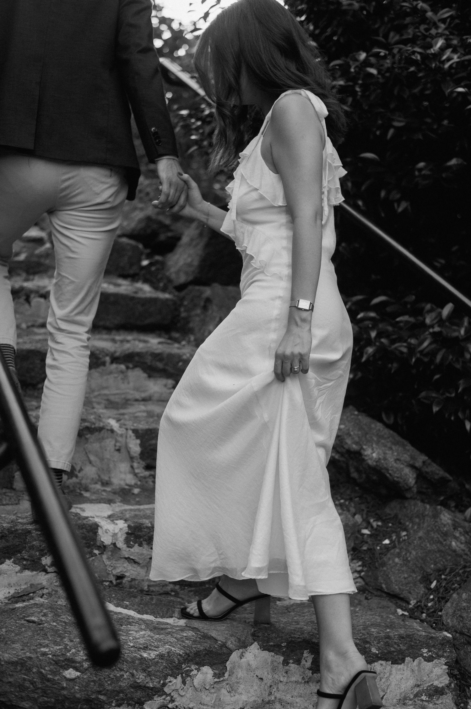 A person in a flowing white dress carefully descends stone steps outdoors in a black and white photograph.