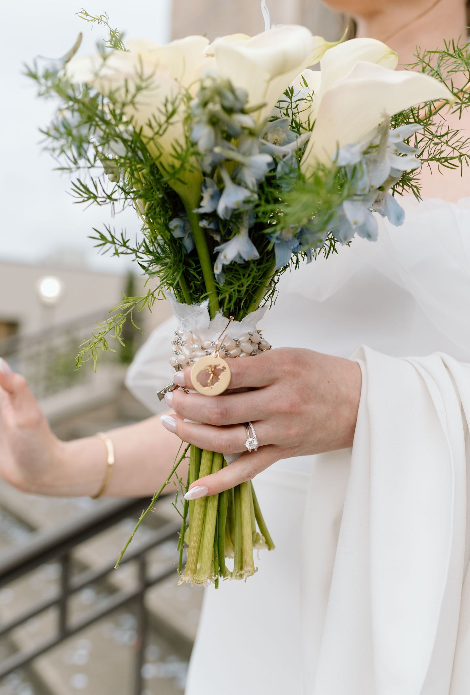 Close-up of a bridal bouquet with white roses and delicate greenery held by hands wearing an elegant engagement ring.