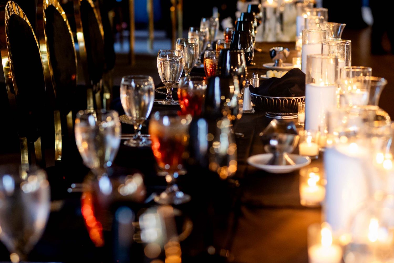 Glowing candlelight illuminates a romantic table setting with wine glasses and place settings at an elegant restaurant.