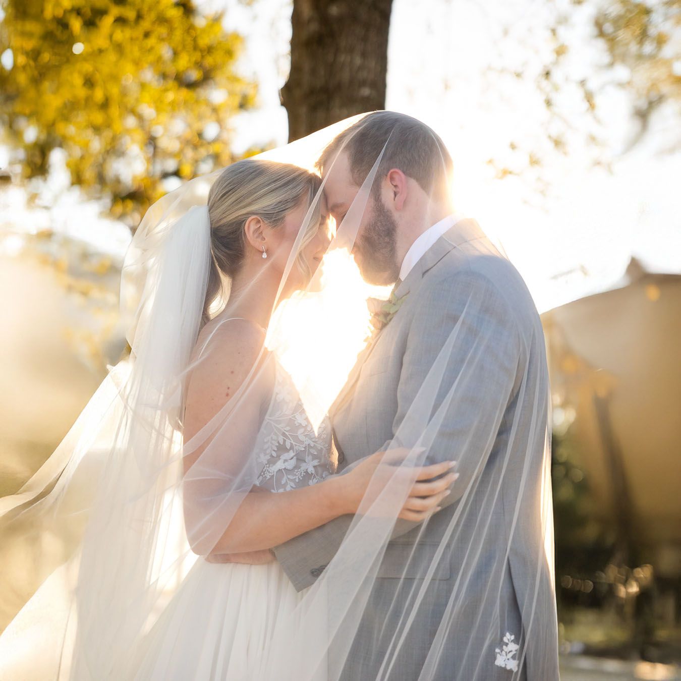 A romantic wedding couple shares an intimate moment at sunset with golden light streaming through autumn trees.
