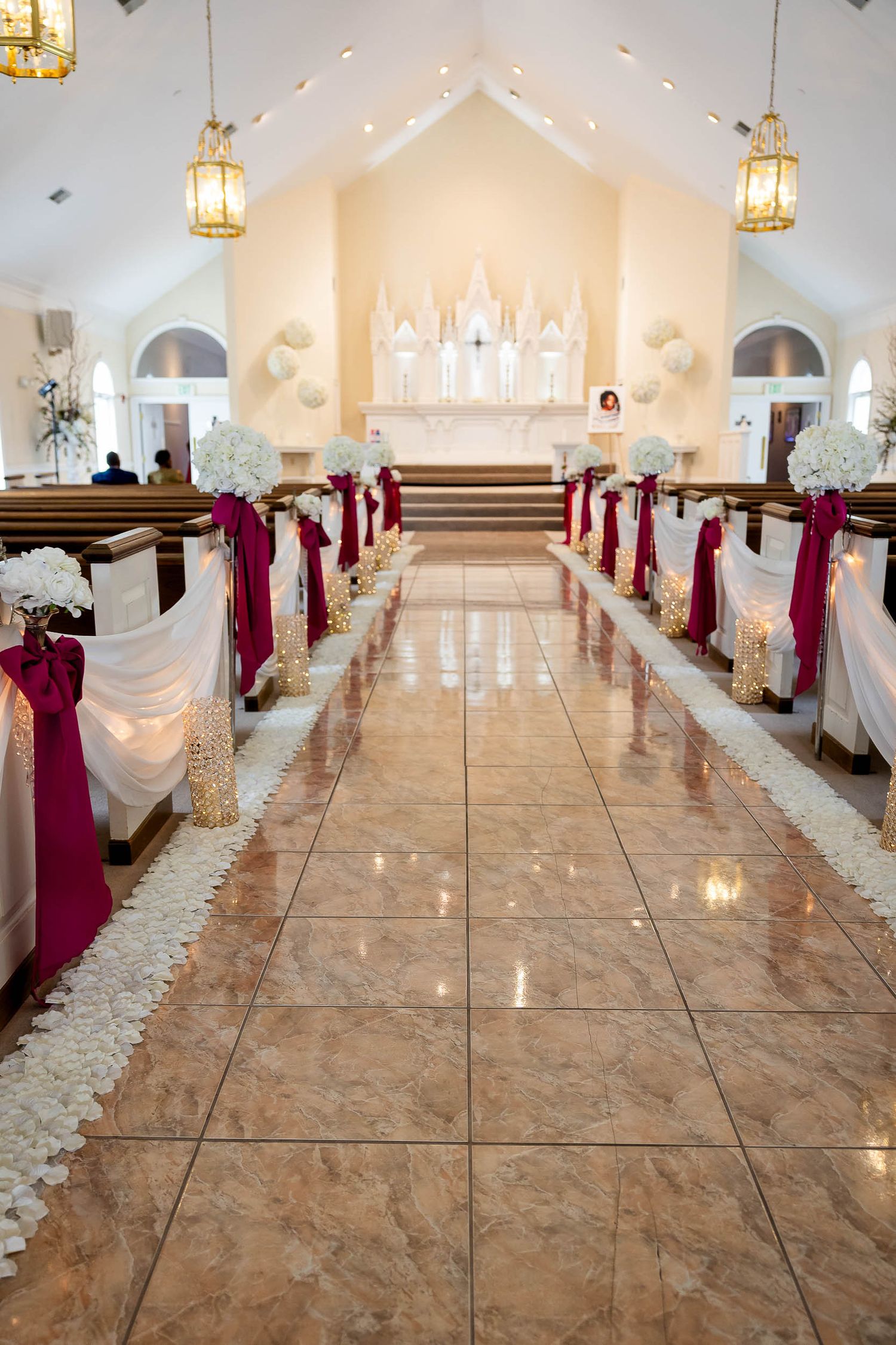 Chapel interior decorated for wedding ceremony with white and burgundy aisle decor and elegant hanging lanterns.