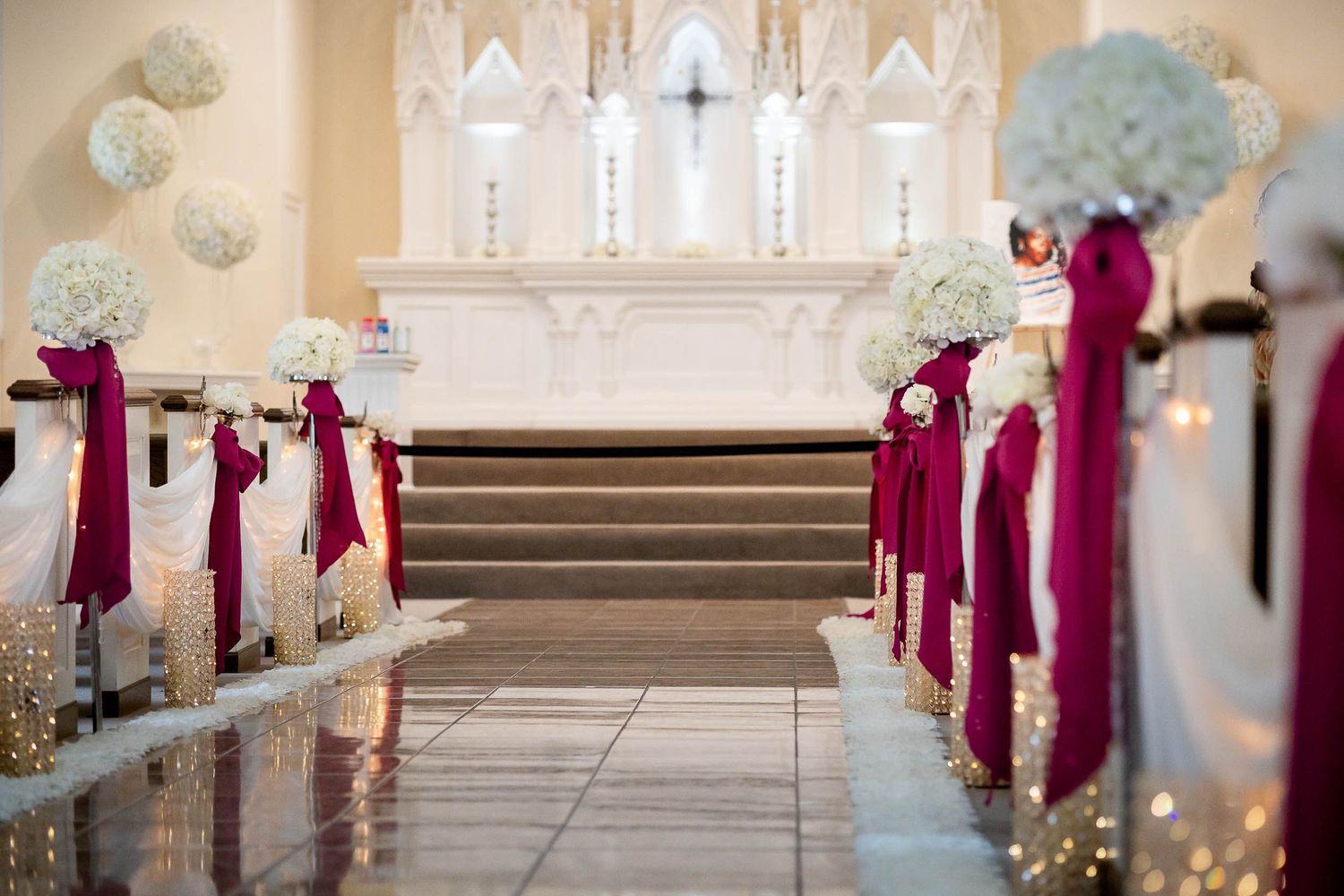 Church altar decorated with burgundy ribbons and white floral arrangements along the aisle for an elegant wedding ceremony.