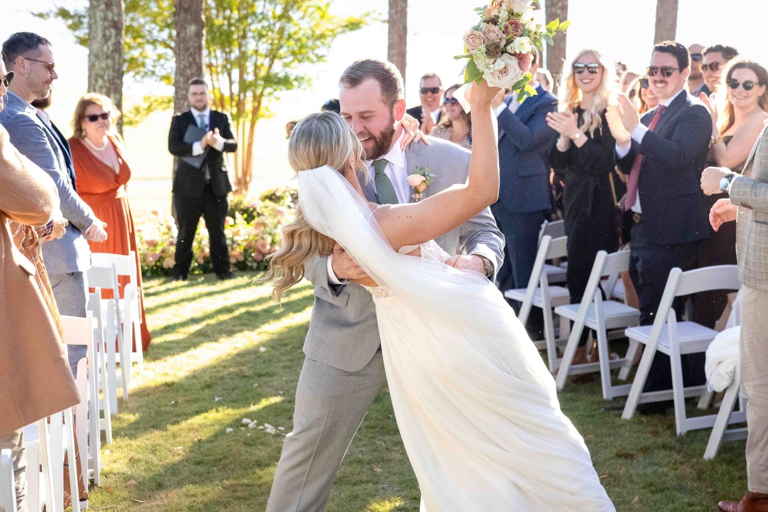 A couple performs a romantic dip during their outdoor wedding ceremony as guests look on and applaud.
