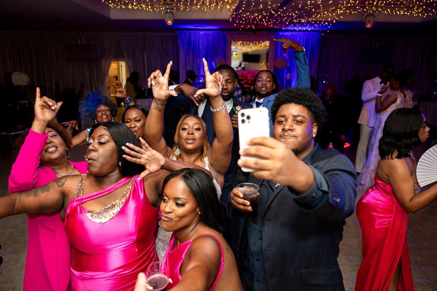 Party guests dance and celebrate enthusiastically at a colorfully lit indoor reception event.