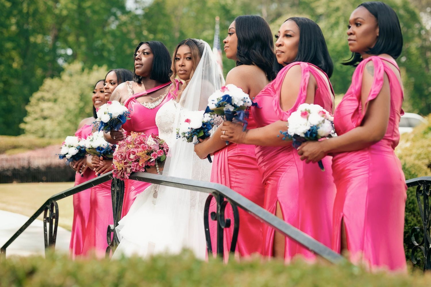 A bridal party of bridesmaids in pink dresses hold bouquets while standing on a bridge.