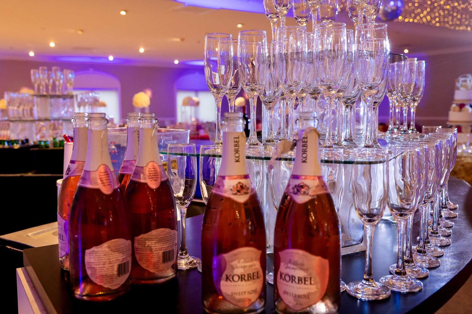 Pink champagne bottles and elegant champagne flutes displayed at a luxurious event bar setup with ambient lighting.