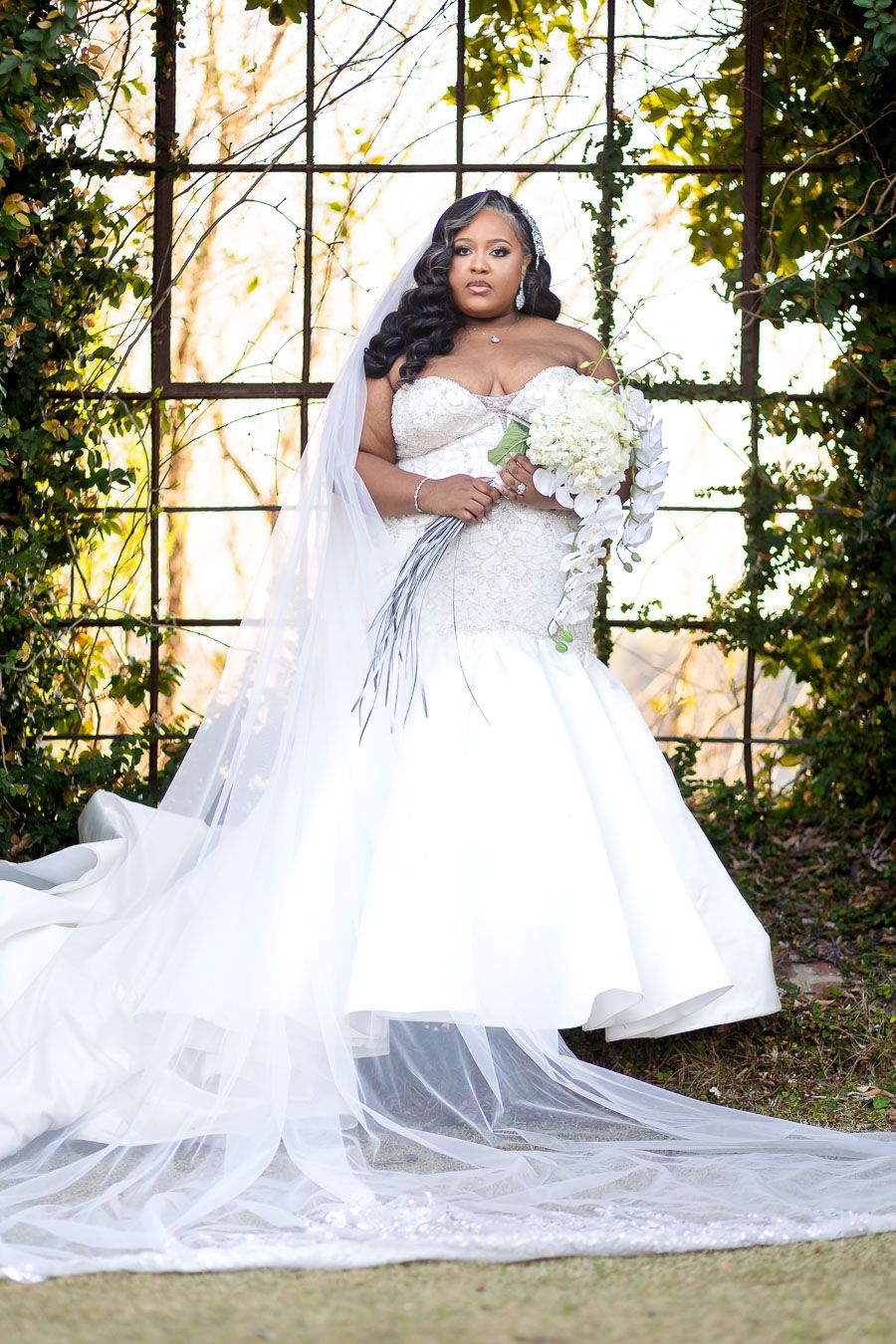 Beautiful off-shoulder white wedding gown with cascading train and veil photographed in outdoor garden setting with natural light.
