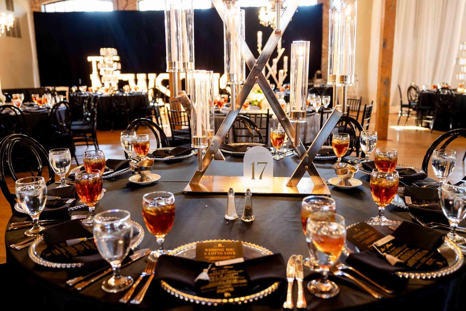 Elegant black and gold wedding reception table setting with tall candelabras and crystal stemware on beaded charger plates.