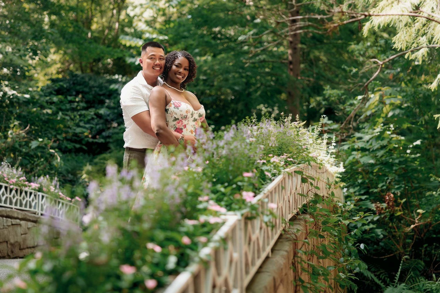 A couple stands on a beautiful garden bridge surrounded by lush greenery and delicate wildflowers.