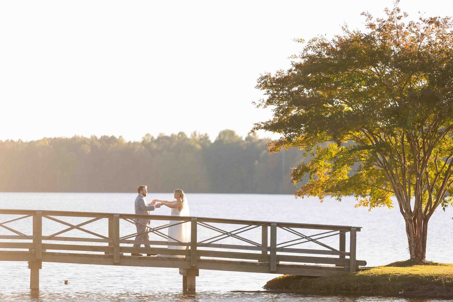 Silhouette of a couple sitting on a wooden dock at sunset with golden light filtering through autumn trees by the lake.