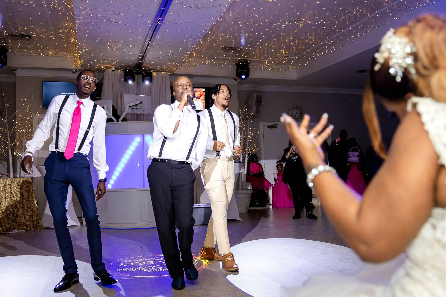 Wedding guests dancing and enjoying themselves on a reception dance floor with festive lighting and decorations.