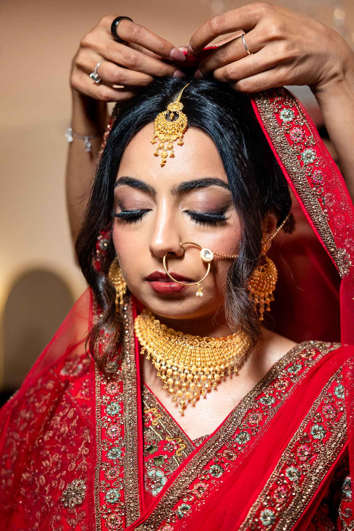 Traditional South Asian bride wearing ornate gold jewelry and red embroidered sari with dramatic bridal makeup.