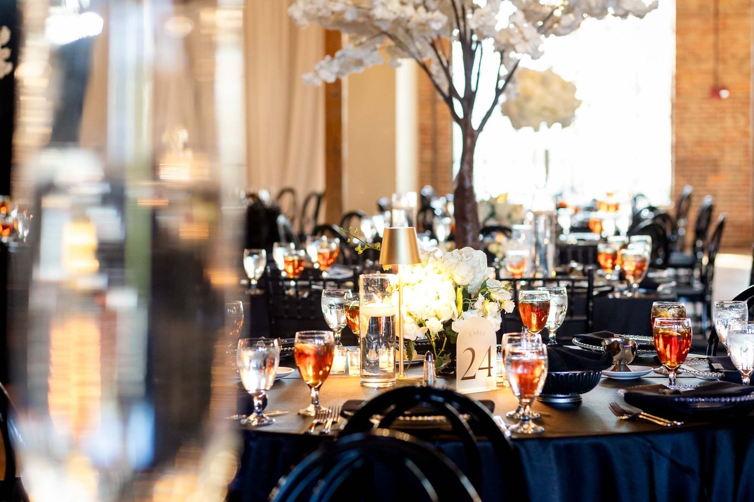 Elegant wedding reception tables decorated with tall white floral centerpieces, navy linens and glowing candle arrangements.