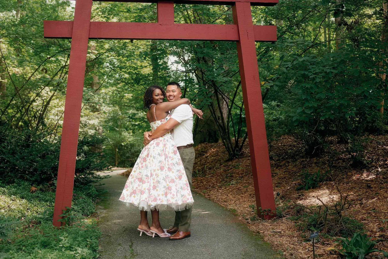 A bright red torii gate frames a serene wooded path through lush green forest scenery.