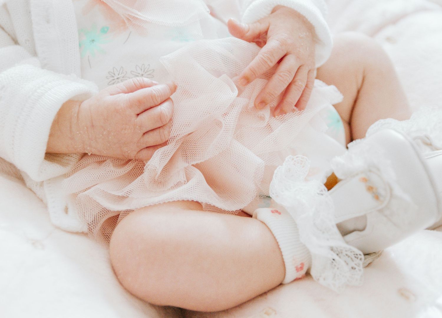 Gentle hands caressing a baby wearing soft white clothing while lying on white bedding.