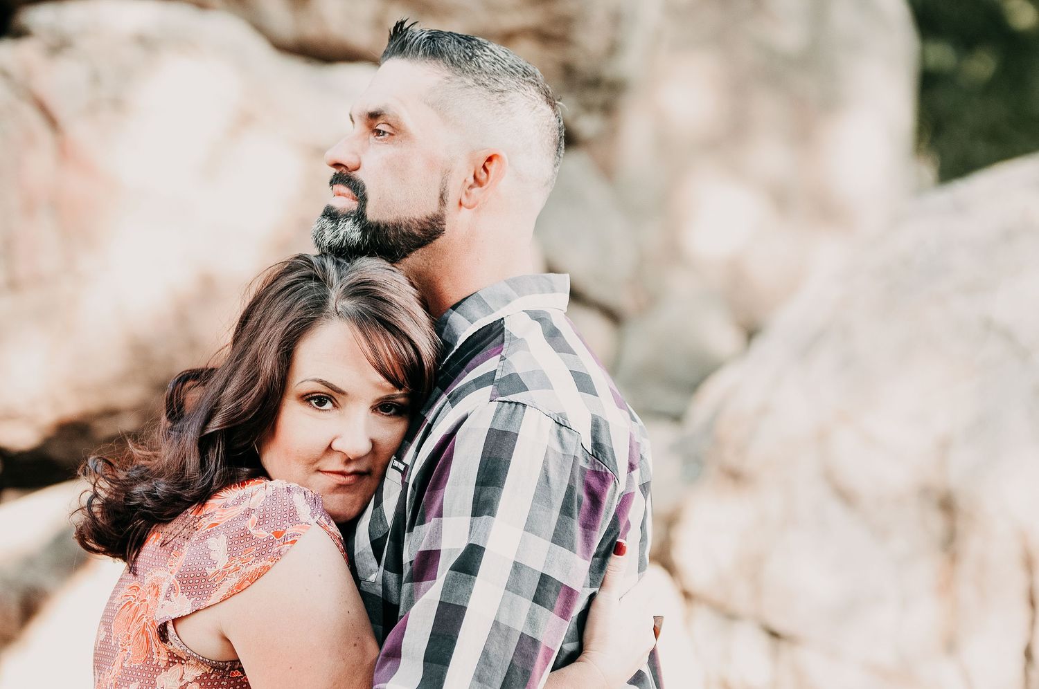 A romantic couple embraces outdoors against a rocky backdrop during an engagement photoshoot.