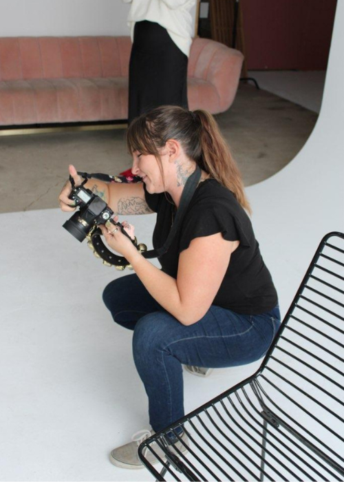 A photographer wearing a black shirt and jeans crouches down with a camera to check the quality of her images in between shots.
