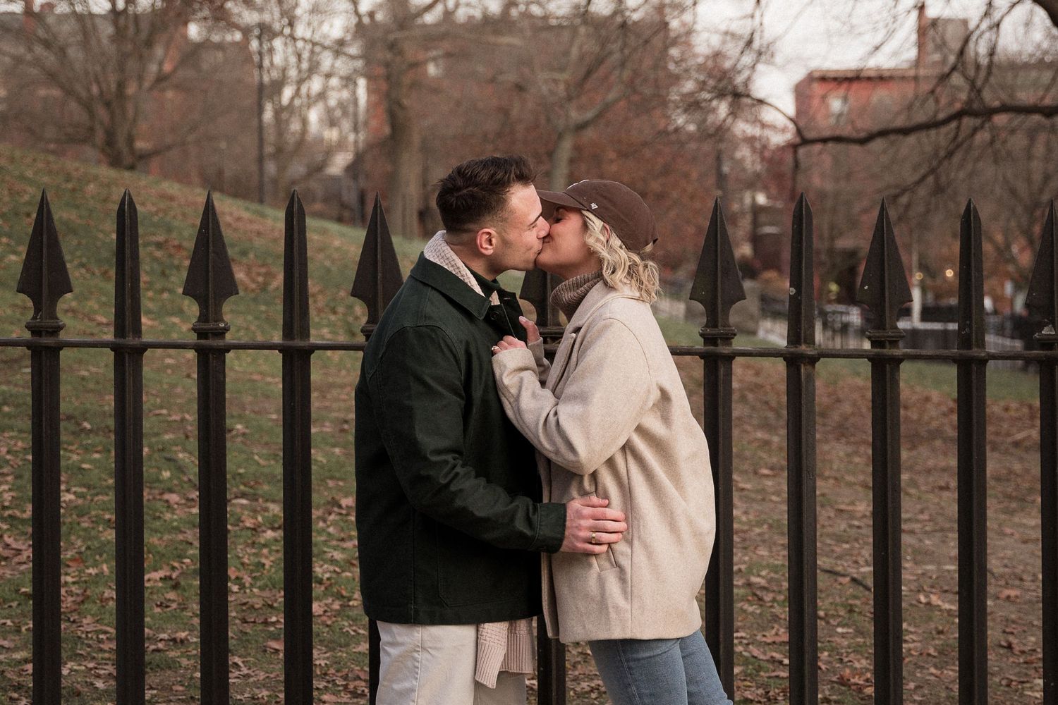 Boston engagement photo of couple kissing in Charlestown park during fall, dressed in stylish city-inspired outfits