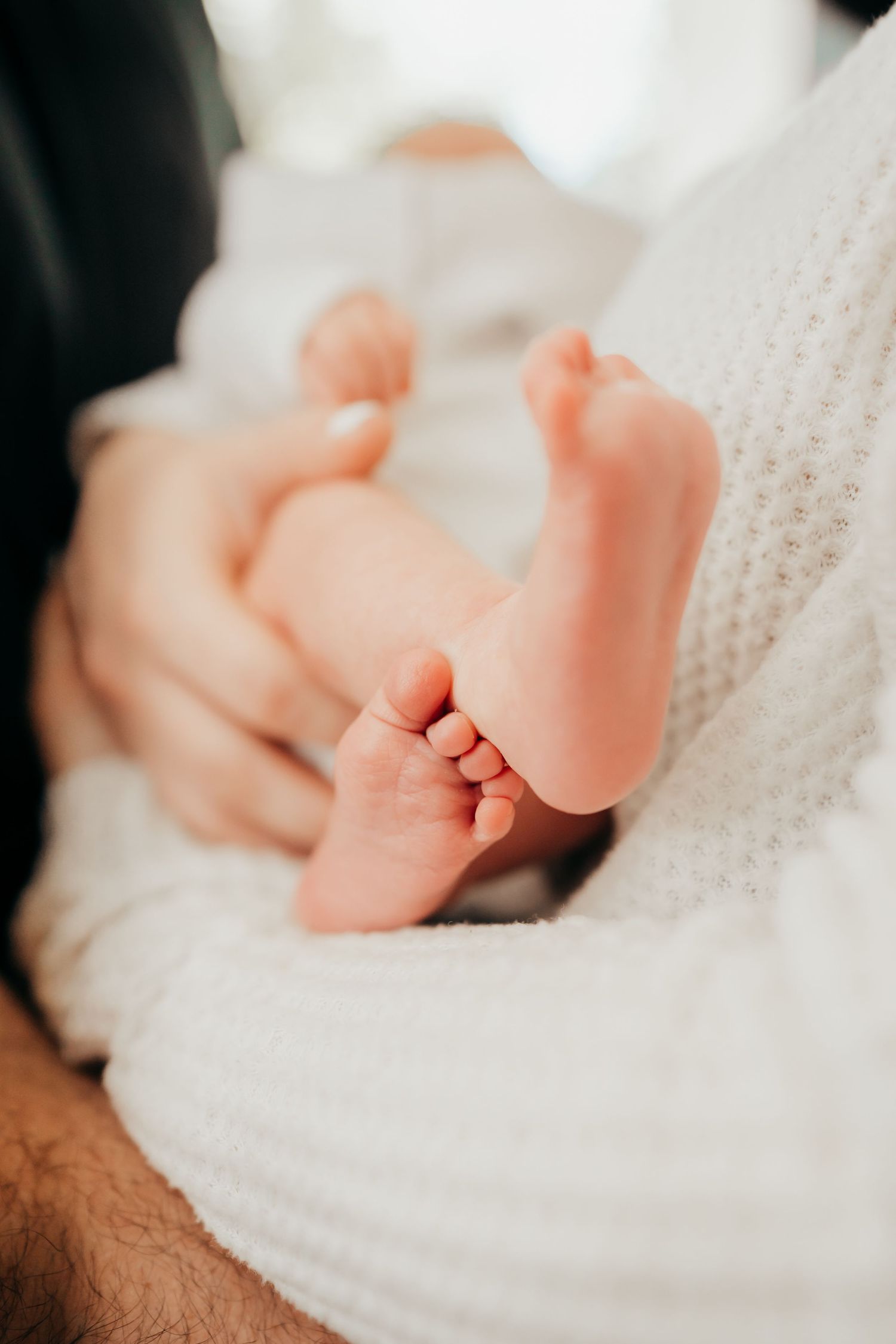 Close-up view of tiny baby feet wrapped in soft white blanket with gentle hands touching.