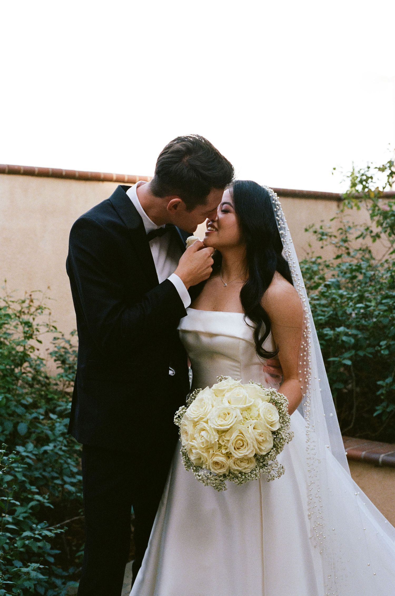 A tender wedding moment captured as a couple shares an intimate embrace while holding a white rose bouquet.