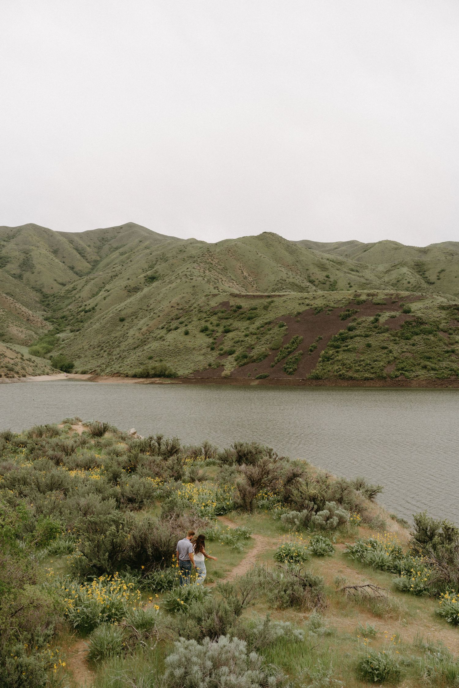 A scenic mountain landscape with a reservoir nestled between green hills and sagebrush in the foreground.