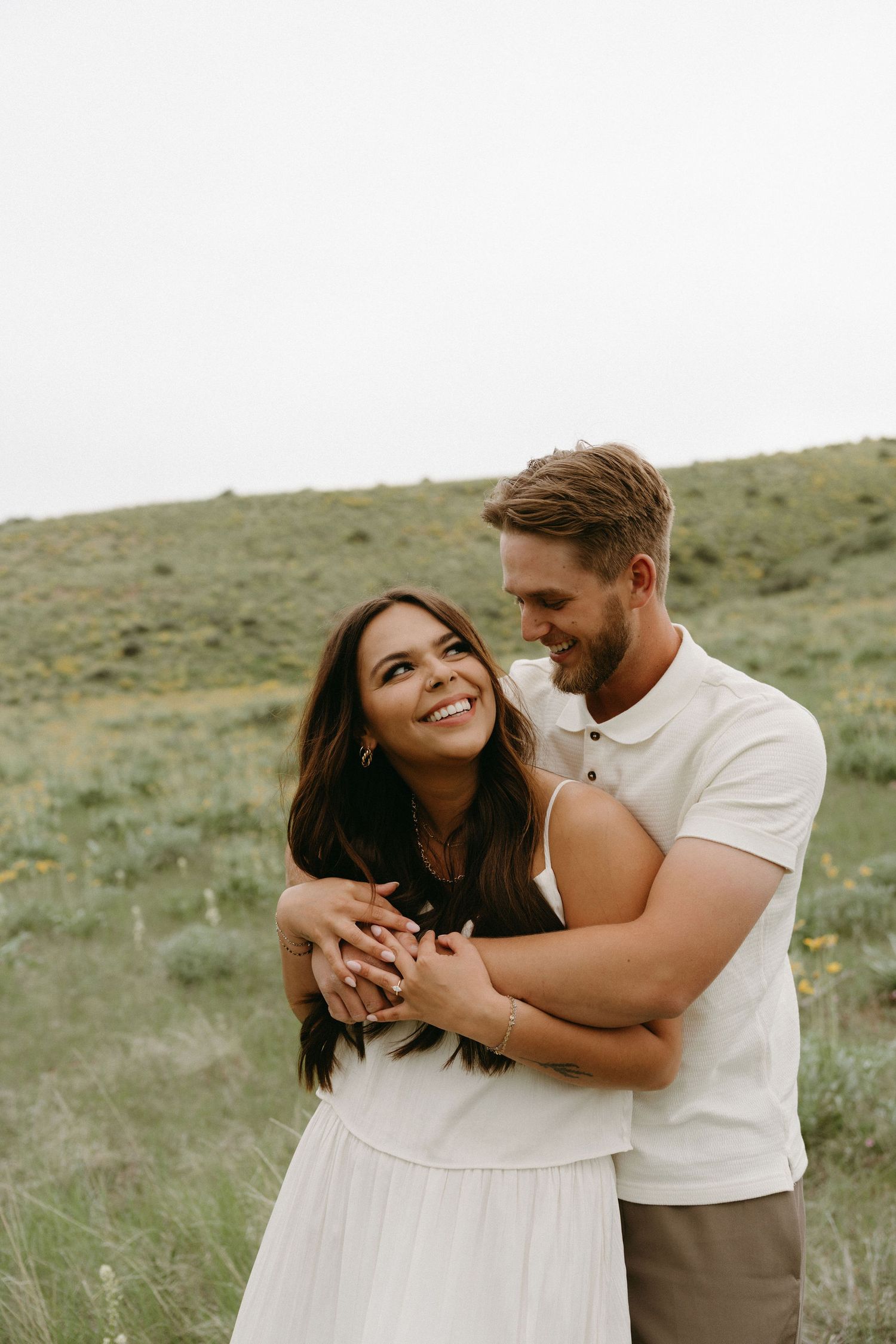 A joyful couple embraces and laughs together in a scenic outdoor setting with rolling hills.