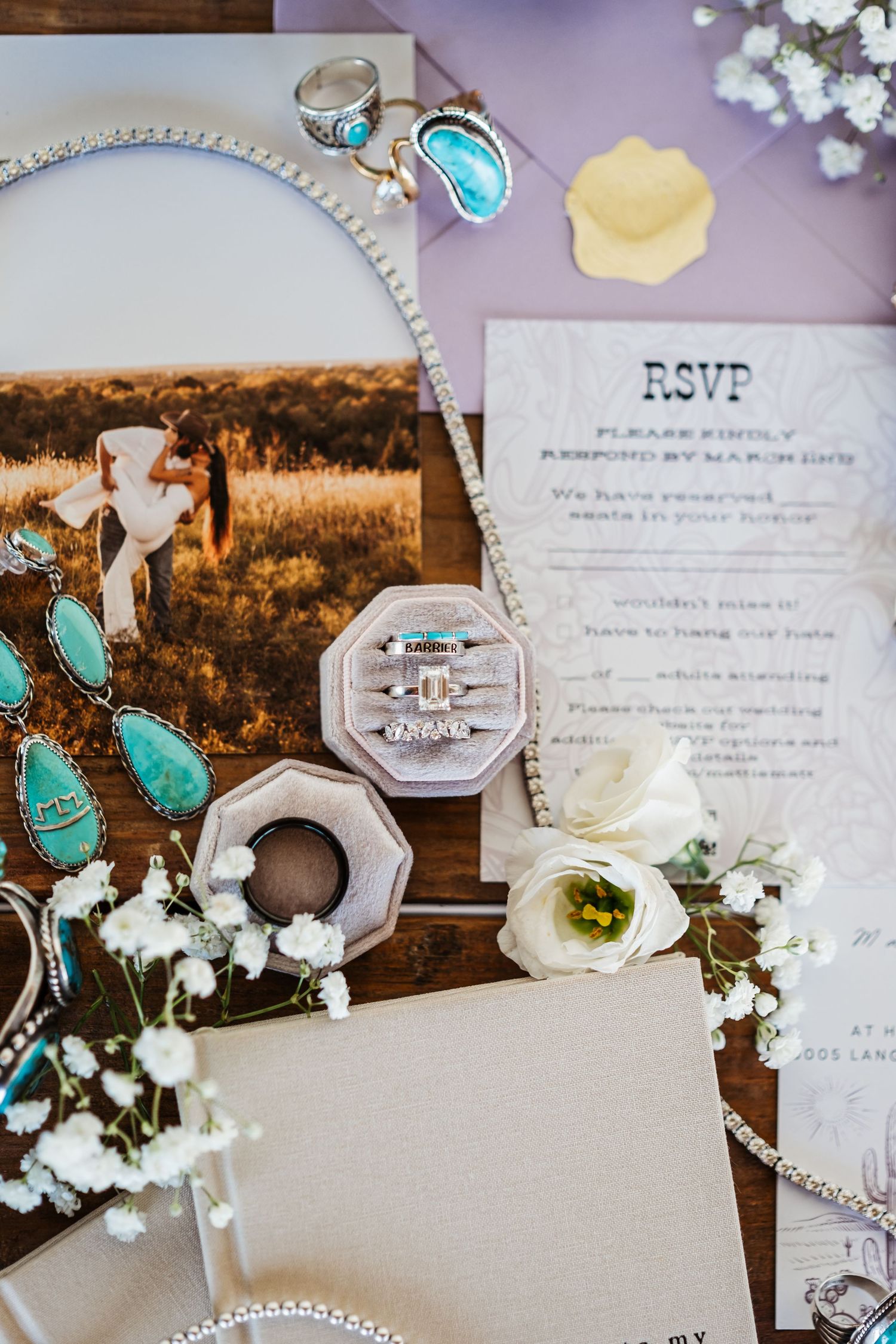 Wedding detail flatlay with turquoise jewelry, RSVP card, white roses and golden sunset photo in rustic style.