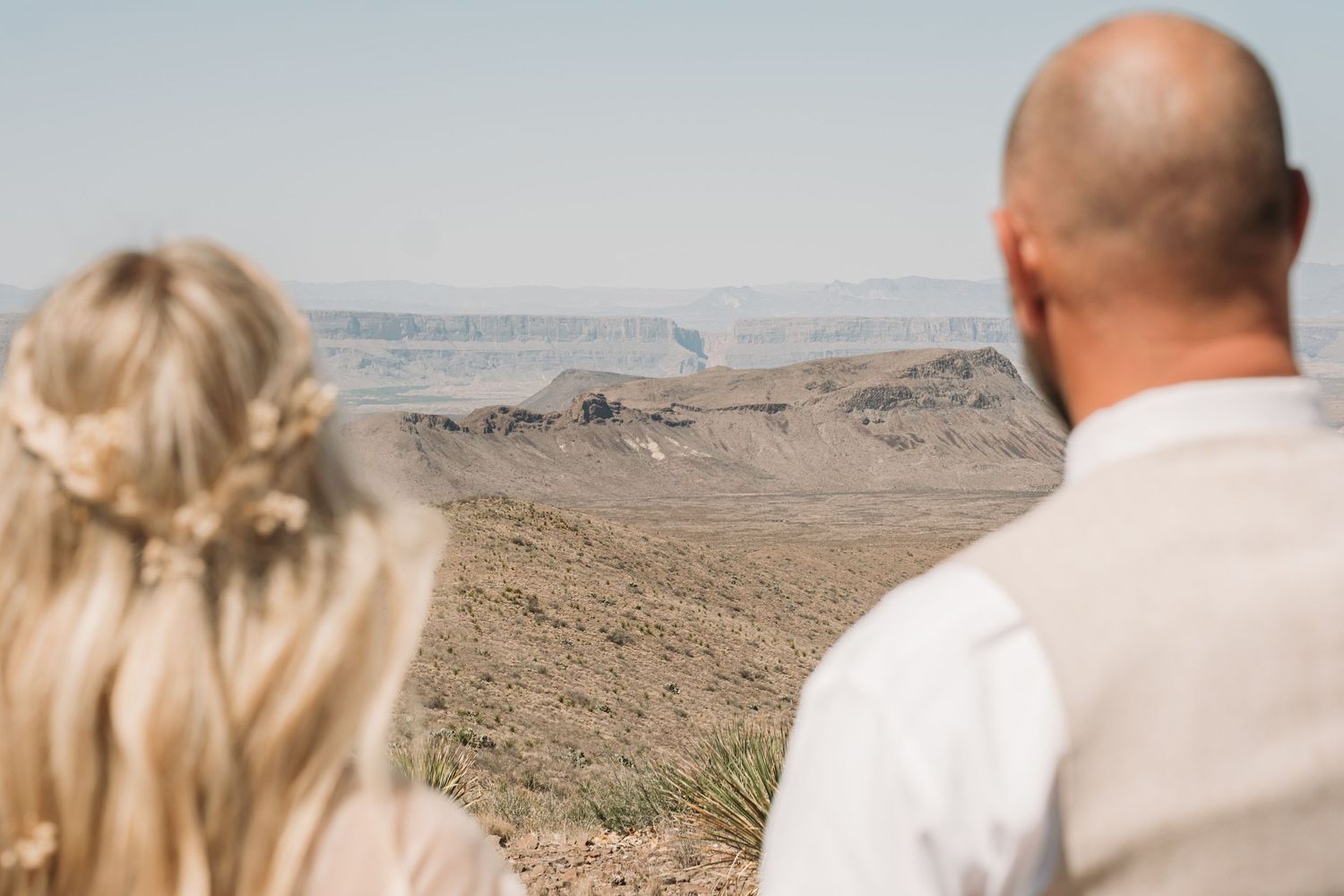 Couple overlooking vast desert landscape from mountainous viewpoint.