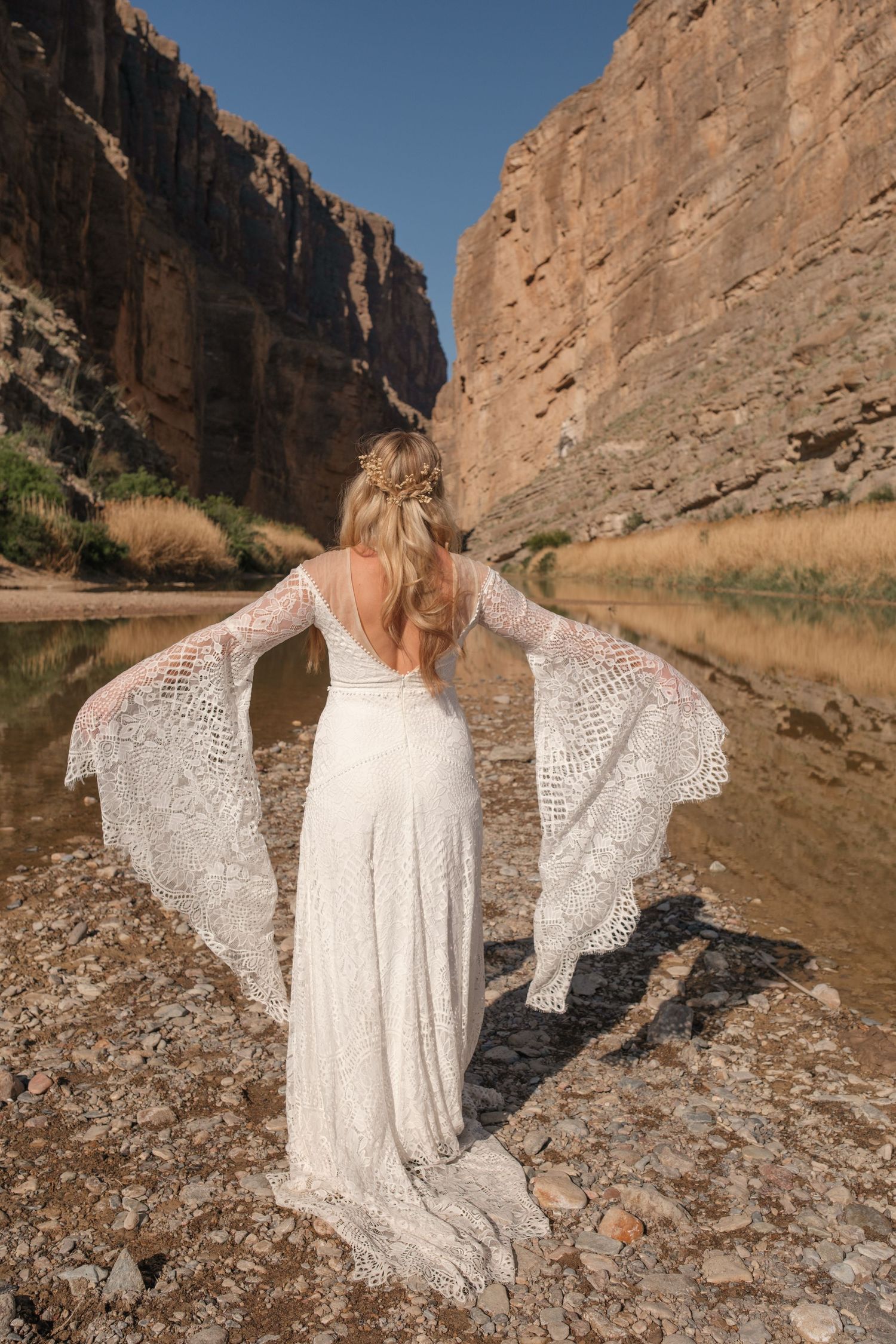 A flowing lace wedding dress catches light in a dramatic canyon setting.