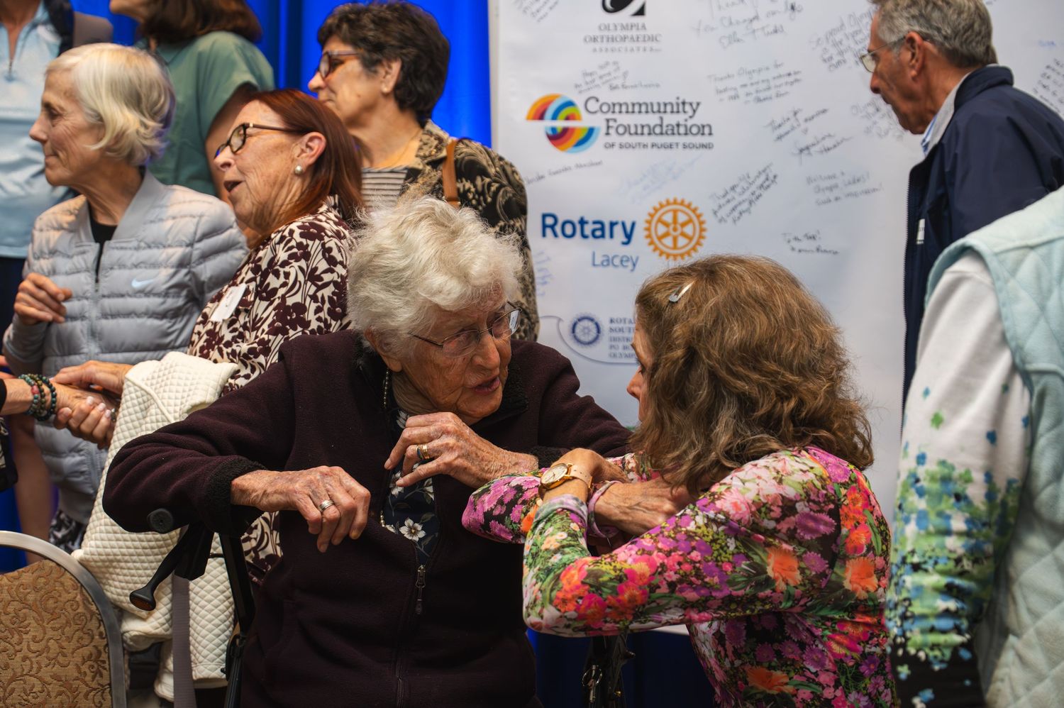 Group of people seated at tables during a formal event with Rotary Club signage visible.