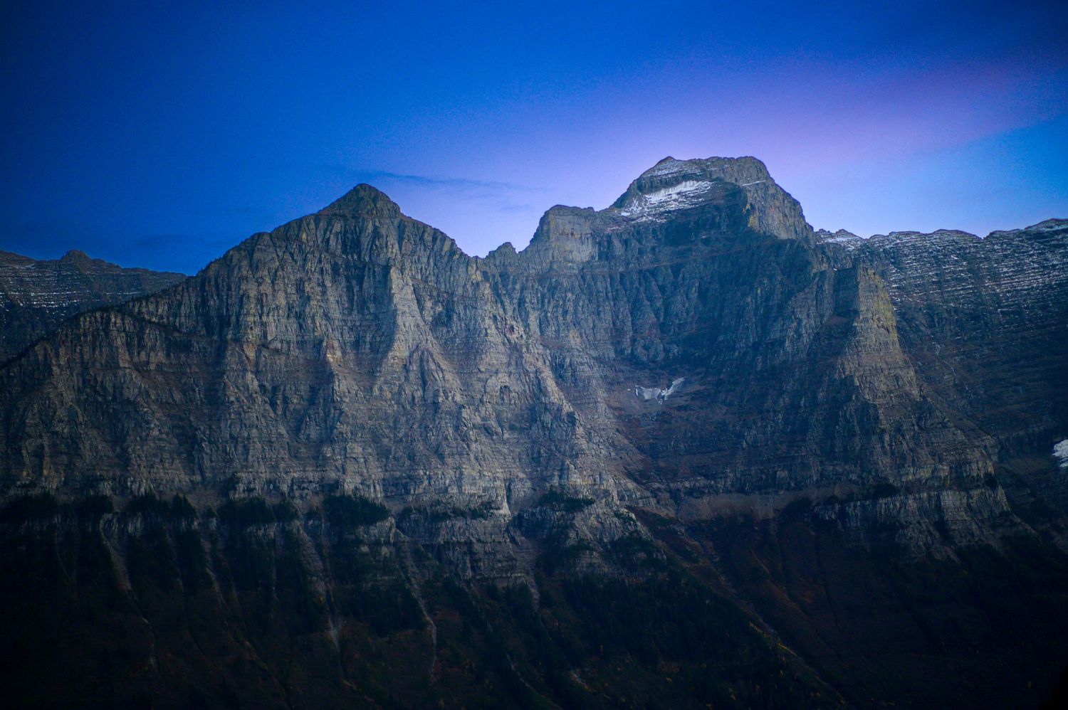 Massive rocky mountain cliffs rise against purple twilight sky in dramatic vertical layers.