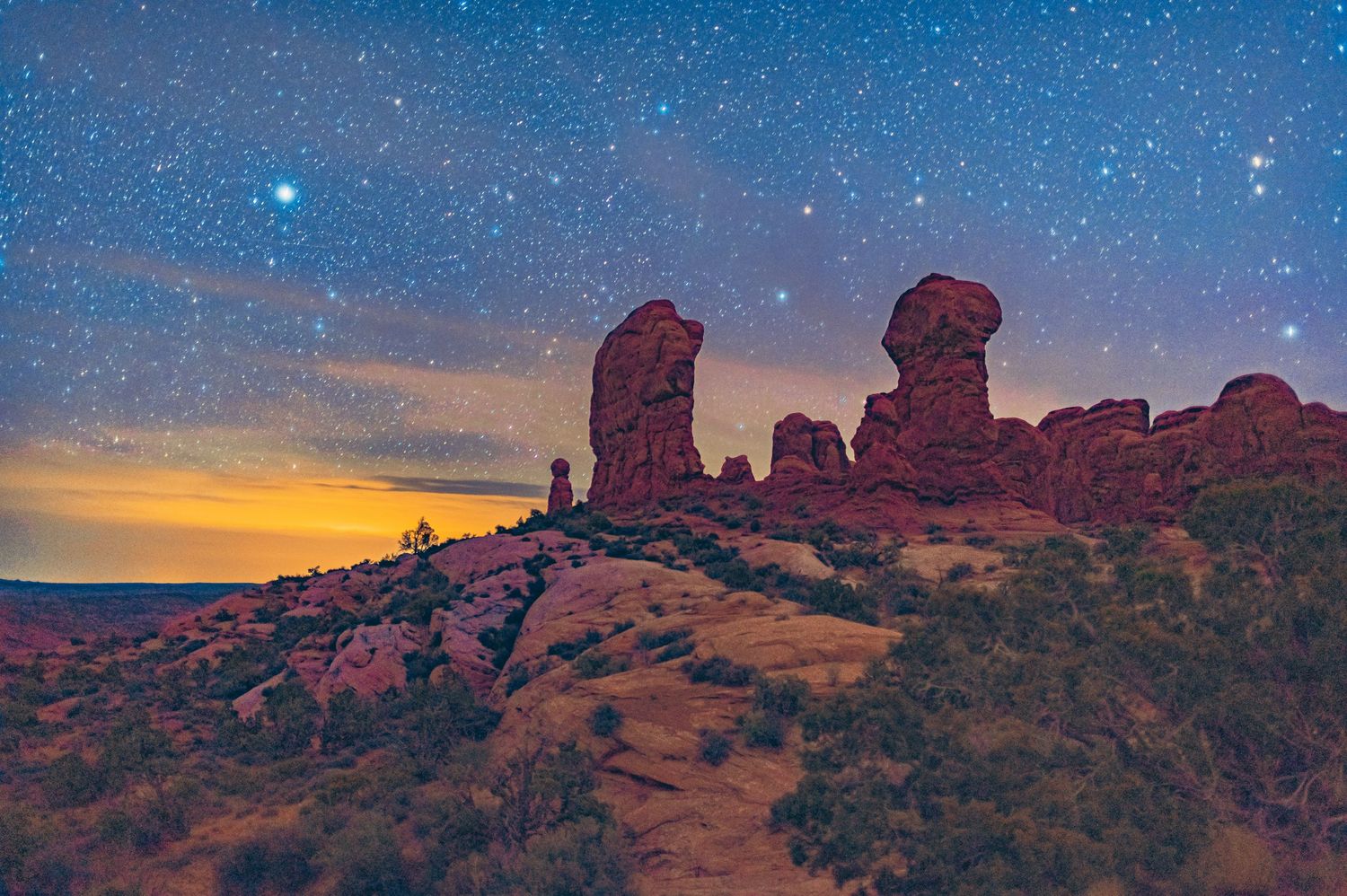 Red rock formations in Arches National Park silhouetted against starry twilight sky.