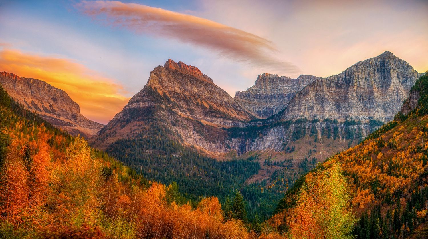 Autumn colors paint mountain peaks golden orange under dramatic sunset skies in a rugged alpine landscape.