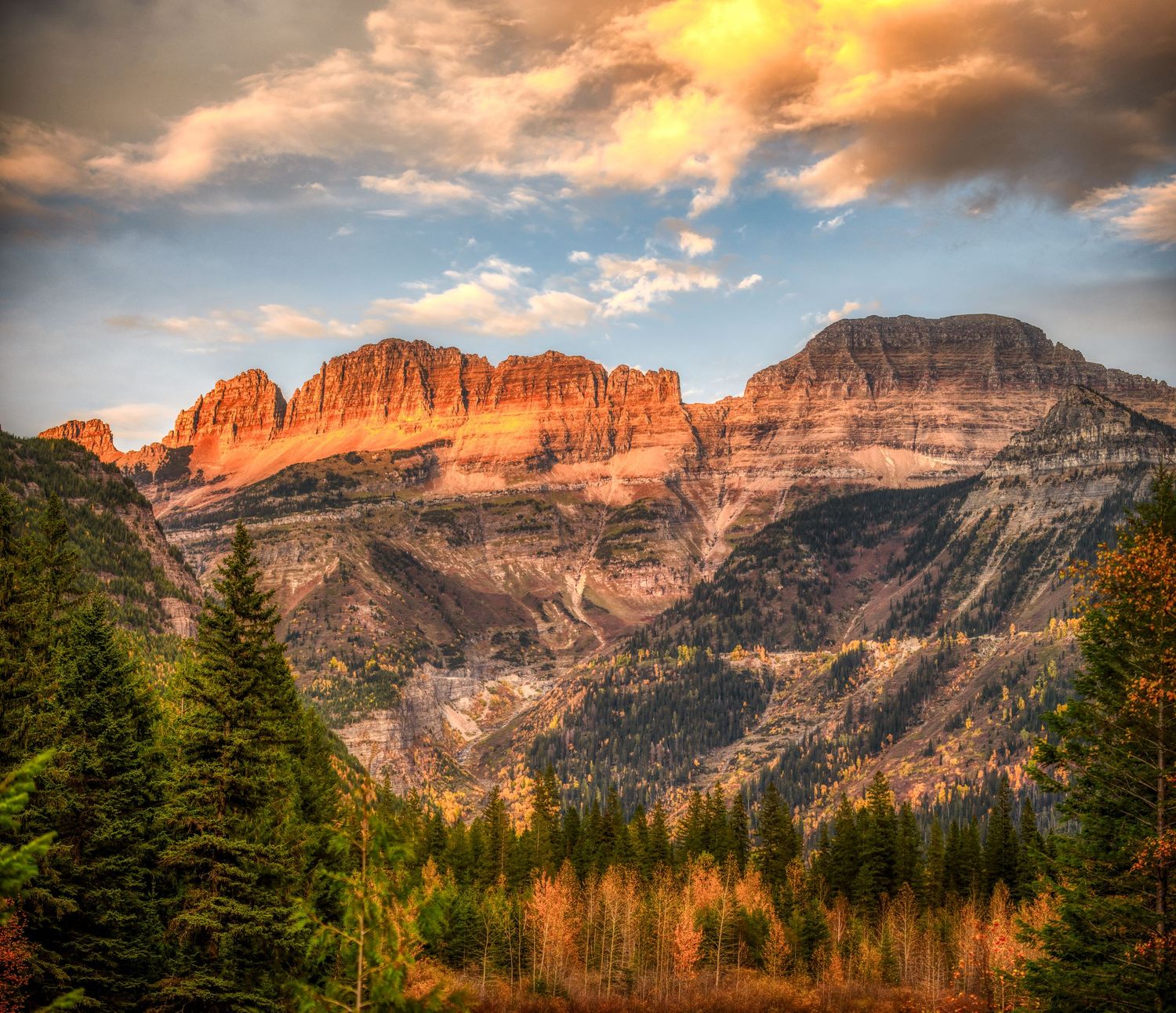 Rugged mountain peaks bathed in warm sunset light above autumn forest in national park.