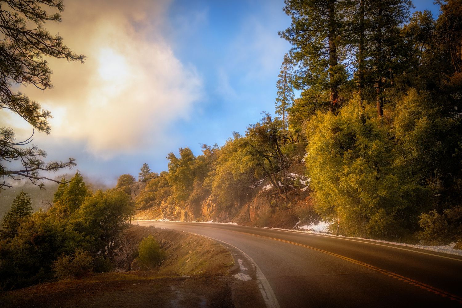 Winding mountain road through autumn forest with sunlit fog and golden foliage.