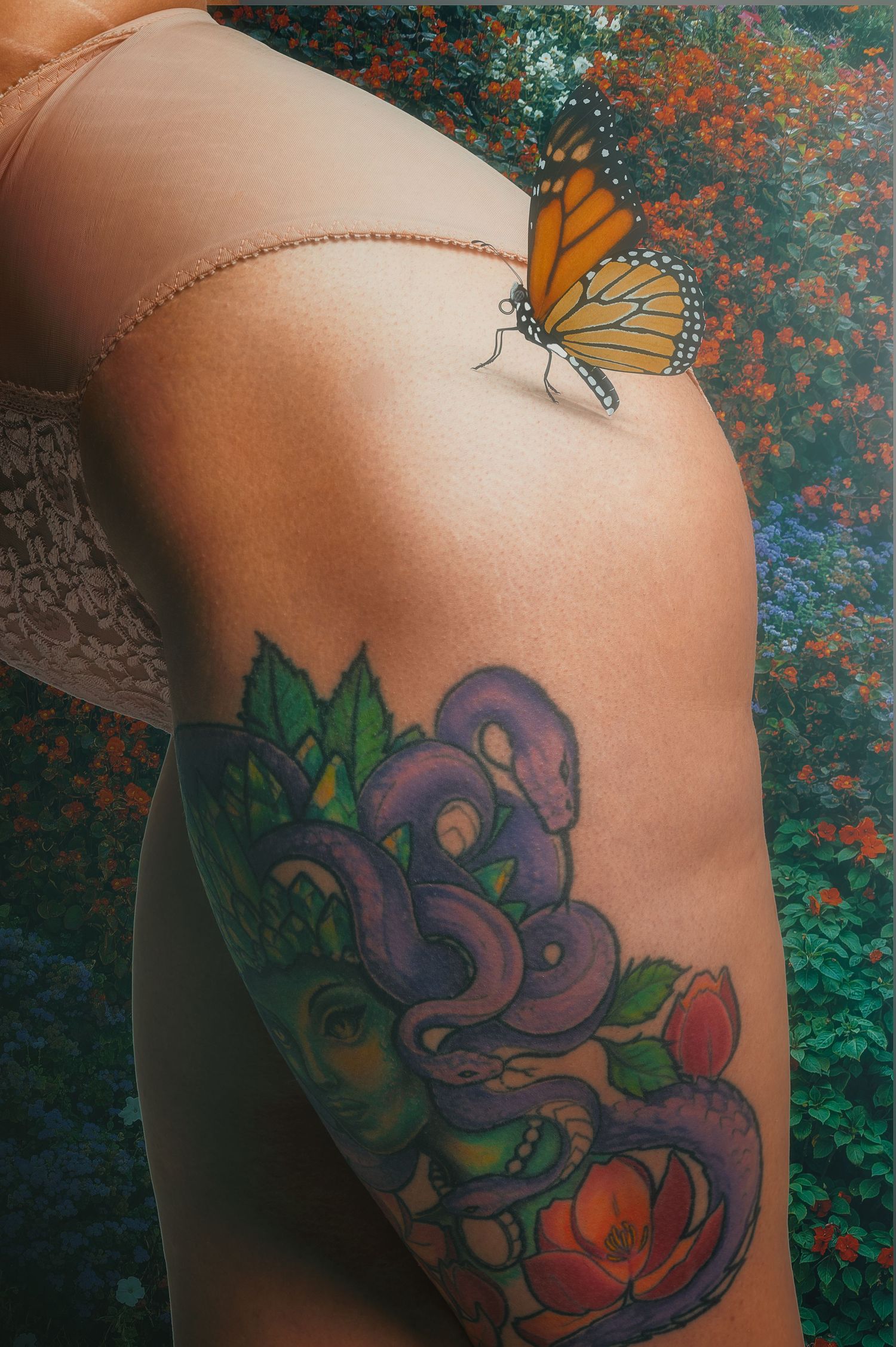 Colorful floral tattoo with monarch butterfly on skin against teal background.