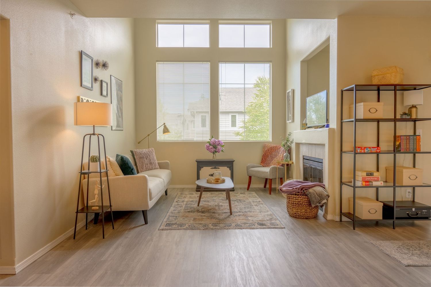 Modern minimalist living room with natural light, grey sofa, wooden floors and industrial-style shelving unit.
