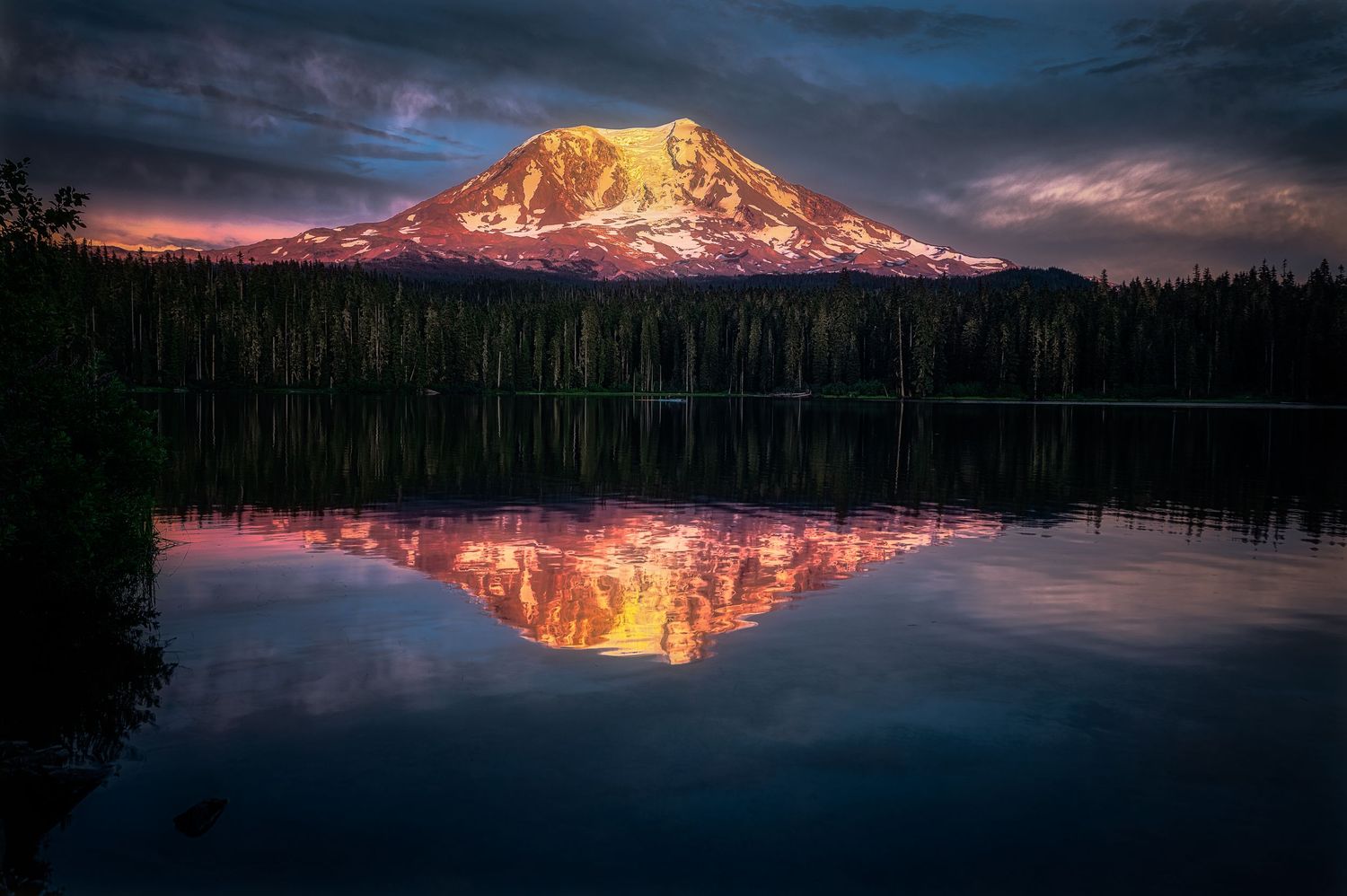 Snow-capped mountain peak reflects perfectly in still lake waters at sunset.
