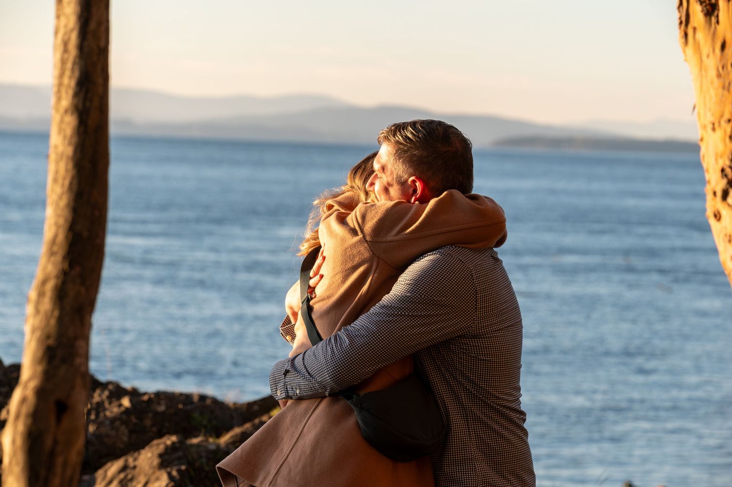 Romantic embrace between couple against ocean backdrop during sunset.