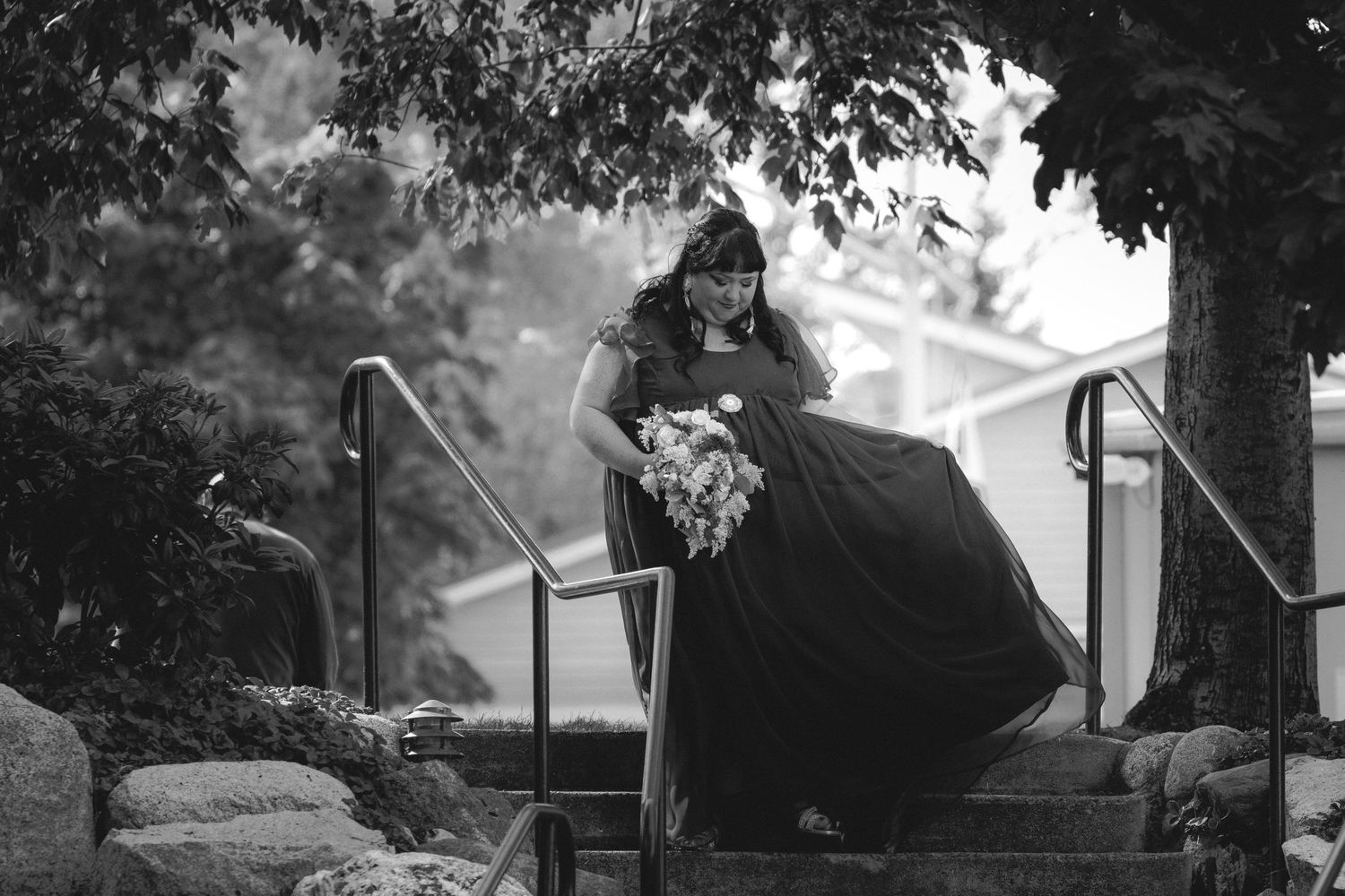 Black and white photo of someone in a flowing dress descending outdoor stairs.