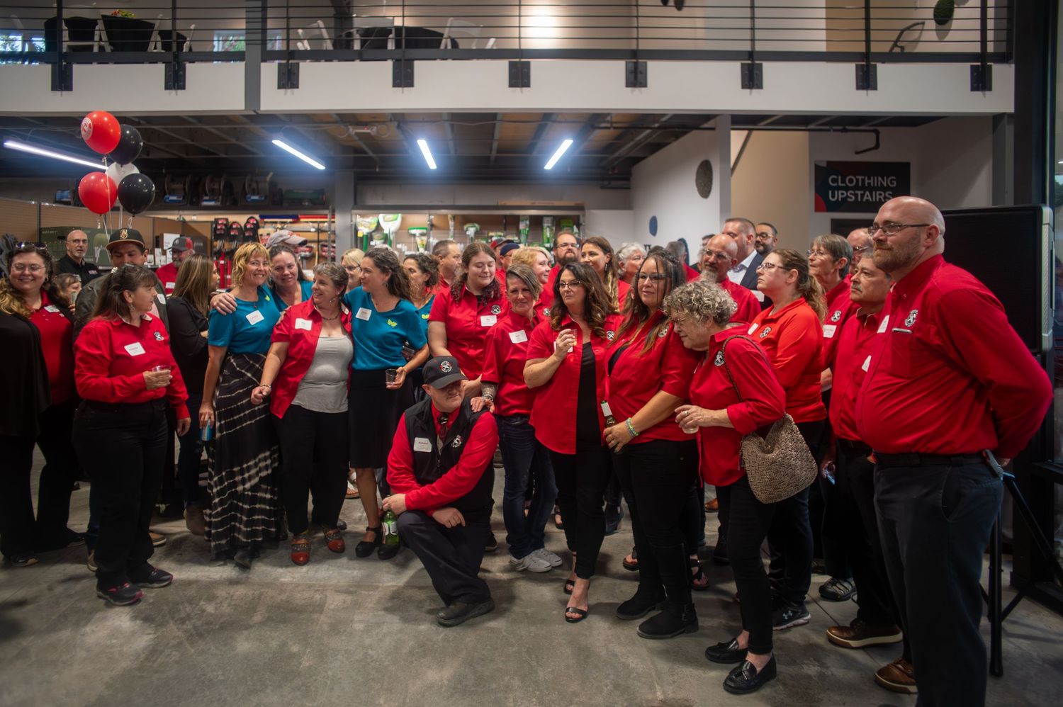 People in matching red shirts assembled in modern industrial building for group photo.