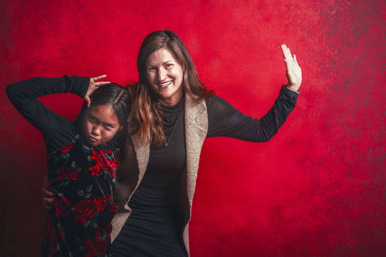 Two people posing playfully against a vibrant red backdrop in casual attire.