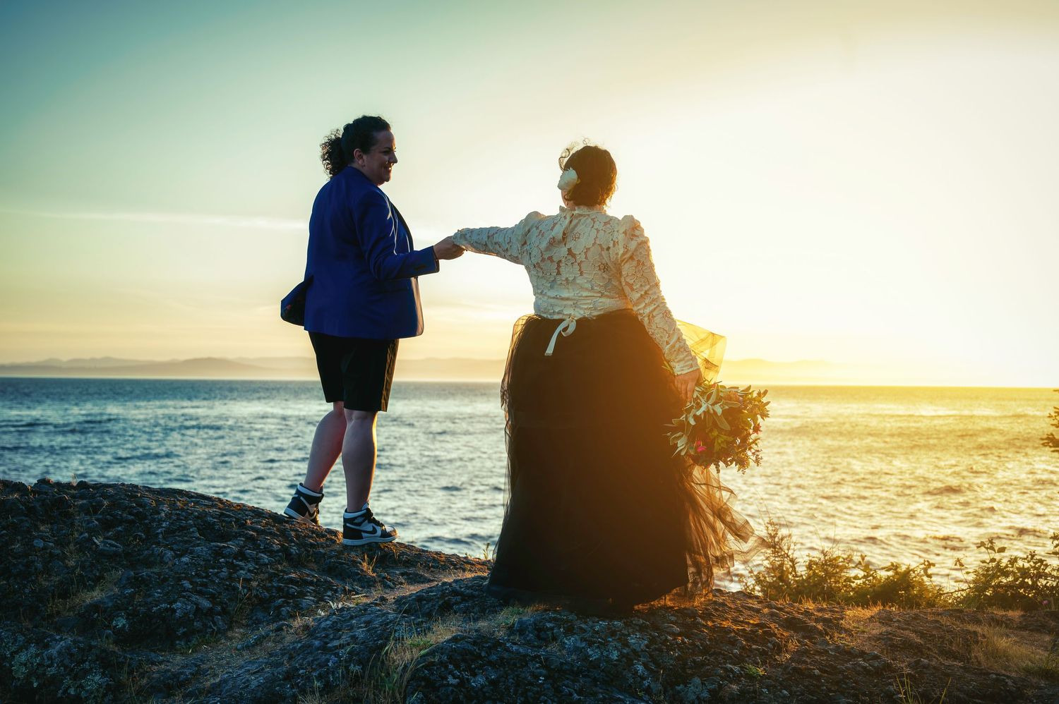 Two people sharing a moment at sunset on coastal rocks by the ocean.