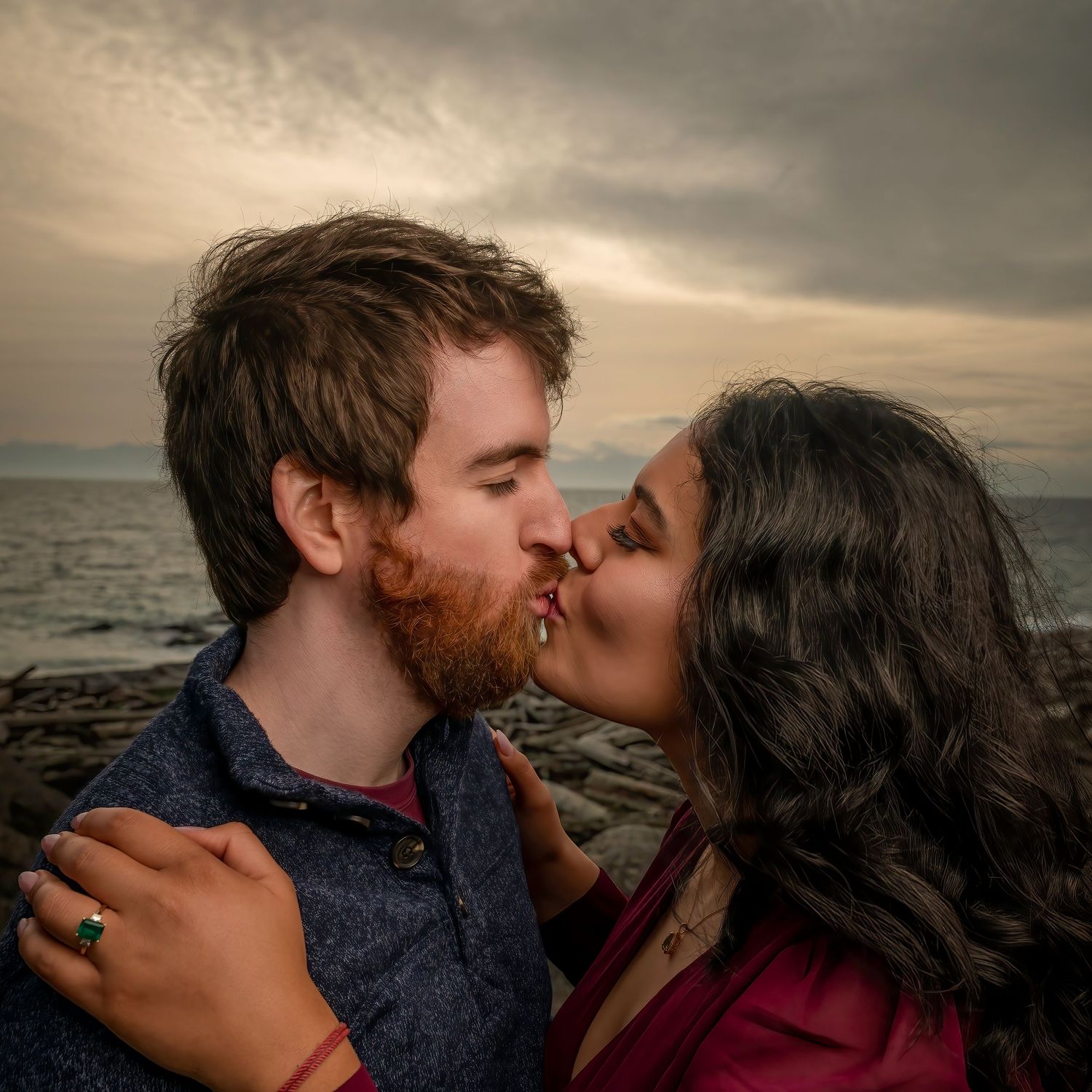 Intimate kiss shared between couple on rocky coastline at sunset.