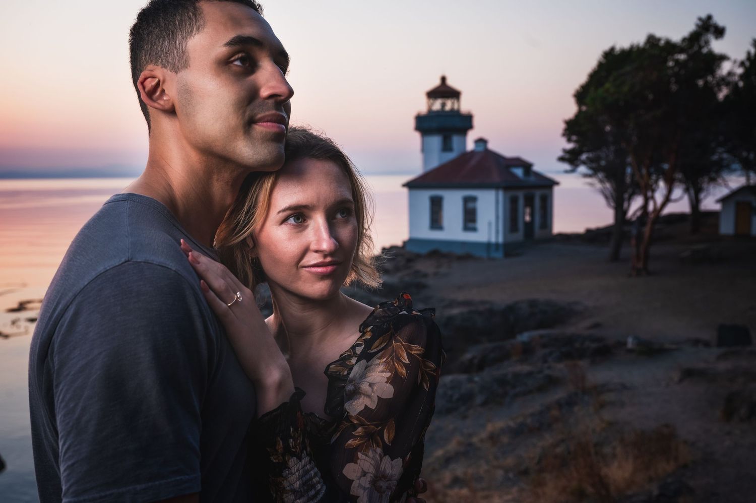 Tender moment between couple with lighthouse visible at dusk.
