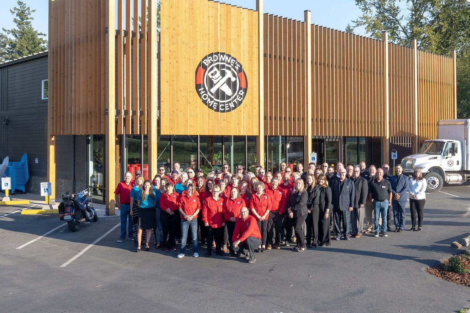 Large group of employees in red and black uniforms gathered outside a modern retail storefront.