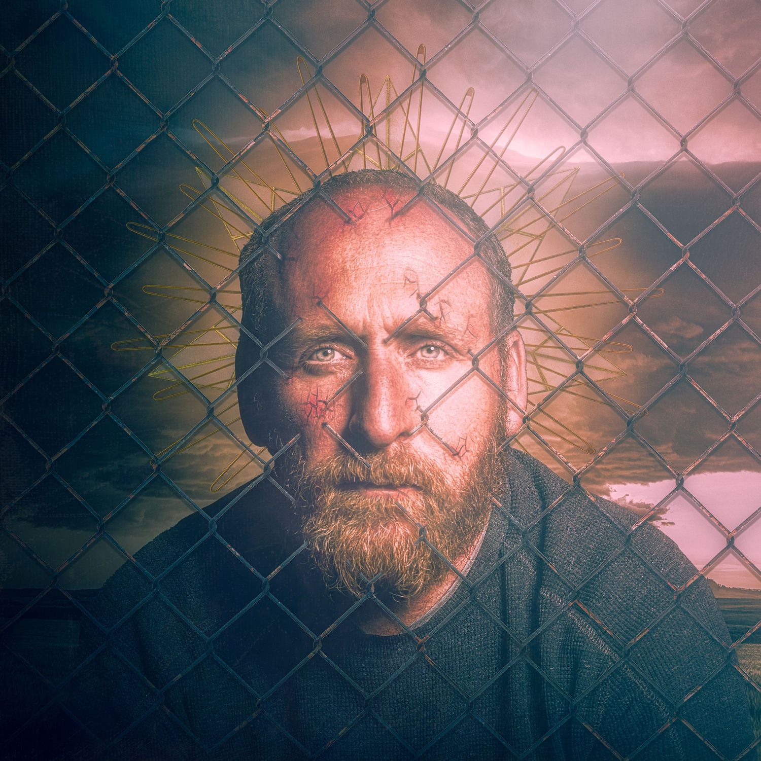 Dramatic portrait with radiating halo effect against chain-link fence background in muted tones.